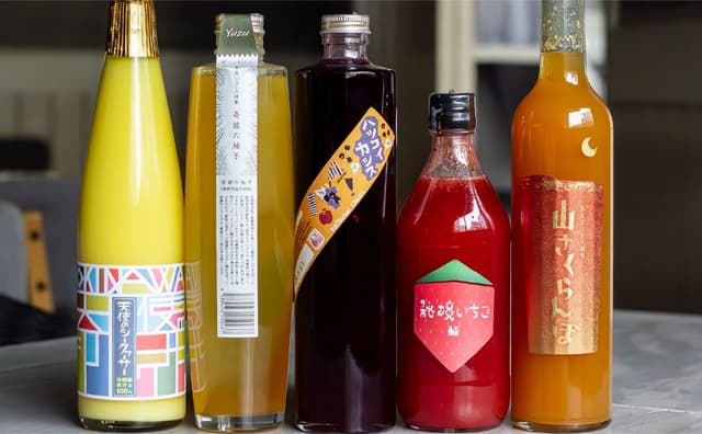ジュースのボトルが5本並んでいる。左から、シークワーサー、柚子、カシス、いちご、山さくらんぼのジュース。